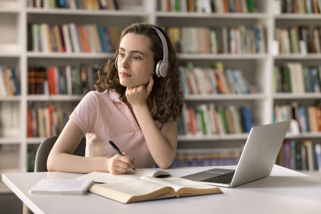 Student listening to headphones while studying with laptop and books